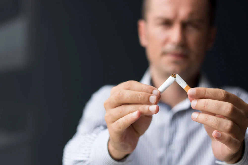 weed-and-tobacco Man breaking a cigarette, symbolizing the dangers of tobacco and the importance of quitting smoking