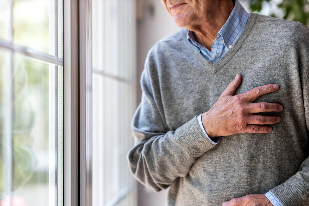 Senior man with chest discomfort near a window showing possible heart damage from drugs