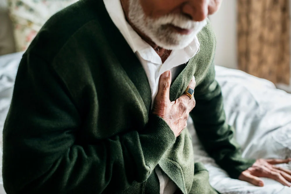 Older man holding his chest while experiencing symptoms of heart damage from drugs