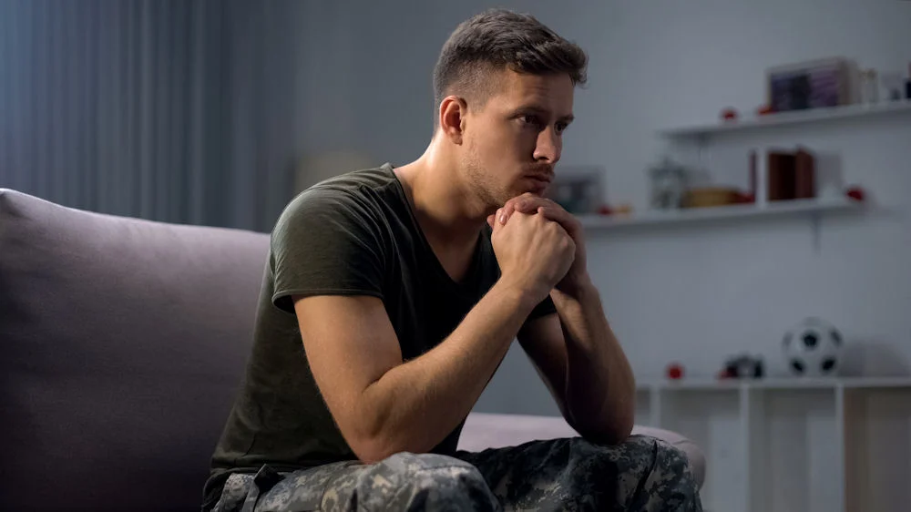 Thoughtful soldier sitting on couch, considering veteran addiction treatment